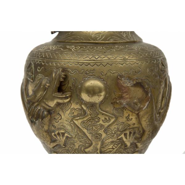 A brass urn with two dragons or serpents facing each other with their mouths open. There is a raised ball in between them.