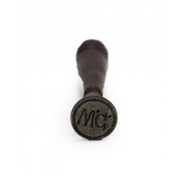 Bottom view of a small letter seal with a wooden handle, showing the initials "W.G." The metal seal is in the shape of a circle. 