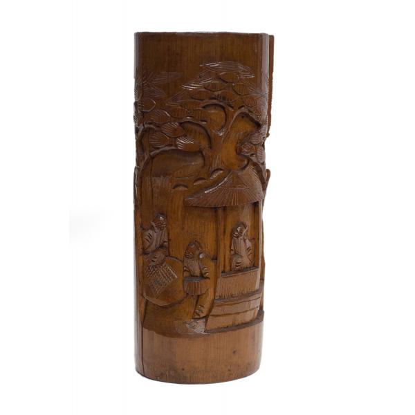 Le devant d’un vase brun en bois sculpté présentant trois hommes près d’une structure couverte et un arbre à l’arrière.