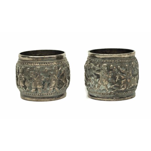 Two silver napkin rings showing figures bringing offerings to a king. 