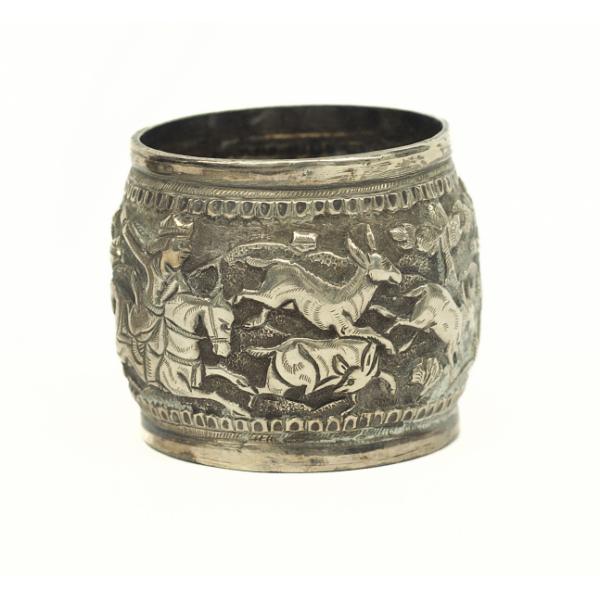 A silver napkin ring showing figures on horseback chasing deer. 