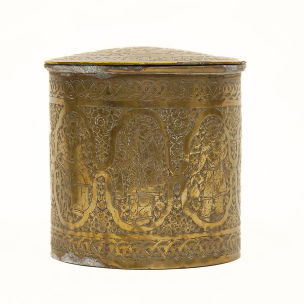 The back of a brass pyxis showing a procession of robed figures surrounded by a floral design.  