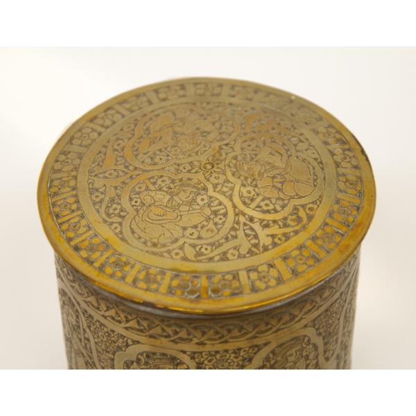 An angled view of the top of a brass pyxis showing the three kneeling figures surrounded by a floral pattern. 