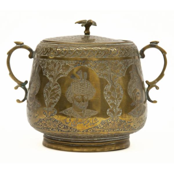 The front of a brass sugar bowl showing three medallions with the faces of bearded sultans. The handles are curved  and there is a bird on top of the lid. 