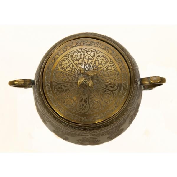 Top view of a sugar bowl showing a floral decoration on the lid. There is a brass bird on top of the lid. The handles of the bowl are curved and are on opposite sides of the bowl