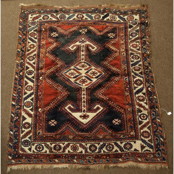 A red Persian rug with black, navy blue, dark yellow, moss green, and white details. There is a geometric design in the centre surrounded by four borders.  