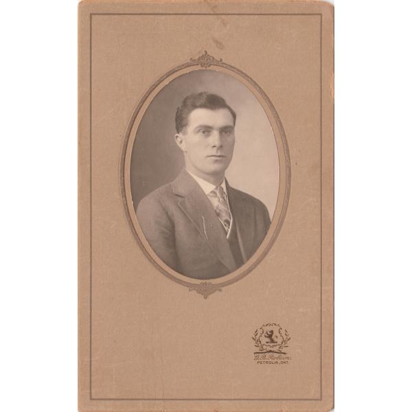 A portrait of Charles Holmes. He is clean-shaven and wearing a suit and tie. The photo is set into a light brown frame with a crest of a lion at the bottom and the inscription "G.B. Robson. Petrolia, Ont."