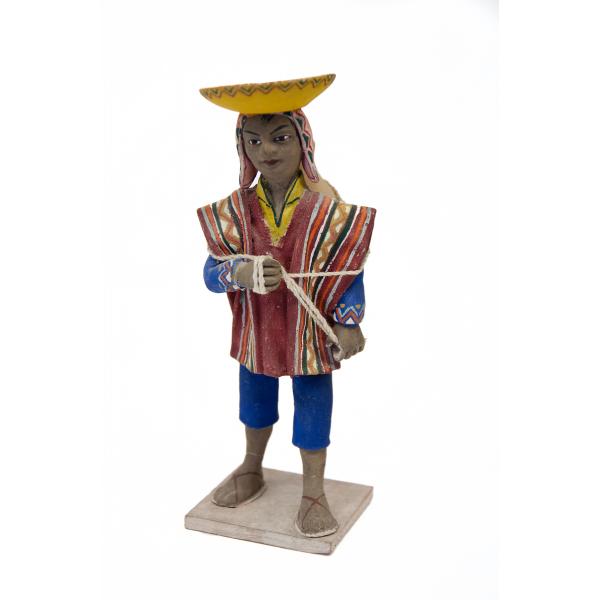 Vue avant de la figurine d’une femme portant une cruche d’eau sur son dos. Elle porte des sandales, un costume bleu et un poncho de différentes couleurs, ainsi qu'un couvre-chef rose et un chapeau retourné jaune et orange.