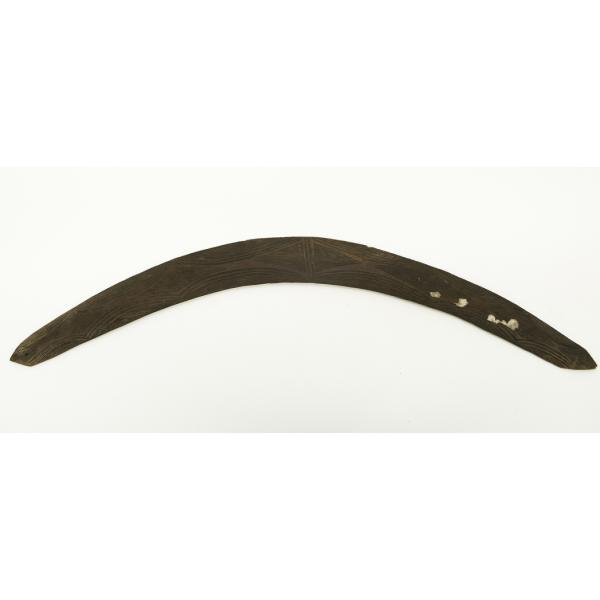 A brown, wooden boomerang. It is curved and there are three holes in one end that are stuffed with paper.  