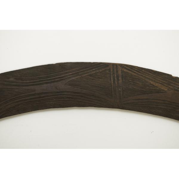 The middle of a dark wooden boomerang, decorated with a pattern of lines.  