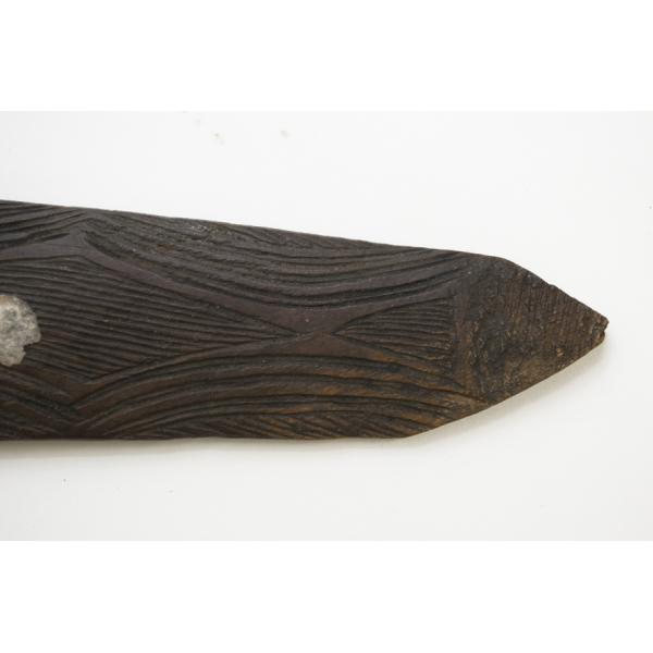 The end of a dark wooden boomerang without a hole in it. There is a line pattern carved into the wood. 