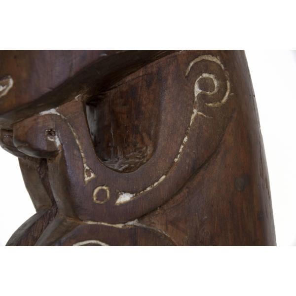 Le bras d'un personnage en bois brun avec un motif de ligne et de cercle sculpté, de couleur plus pâle.  