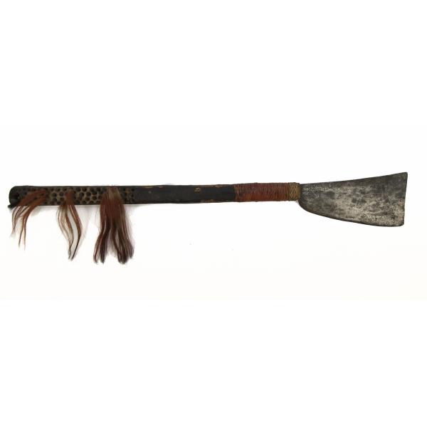 An axe with a short, wide metal blade and a dark wooden handle. The handle has circular holes at the end and three of them are filled with tufts of russet hair. The handle is surrounded by red strings braided near the blade.