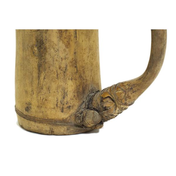 The base of a light brown bamboo pitcher. There is a knot in the wood beside a branch that has been bent to form a handle.