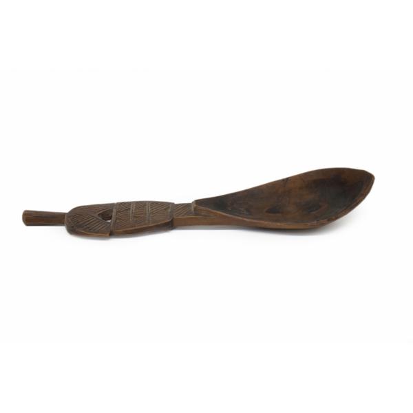 The side of a carved wooden spoon. The spoon is curved and there is a pattern etched into the handle. 