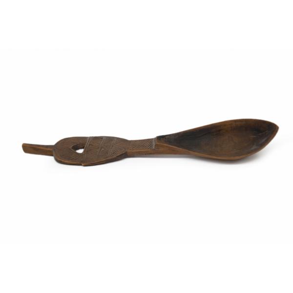 A carved wooden spoon seen from the side. It is slightly curved and there is diagonal hatching on the handle. A stem comes off of the top of the handle.