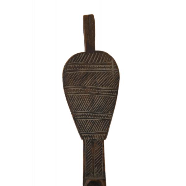 A close-up view of a handle on a carved wooden spoon. It has a stem and is decorated with incised lines and diamond-shapes. 