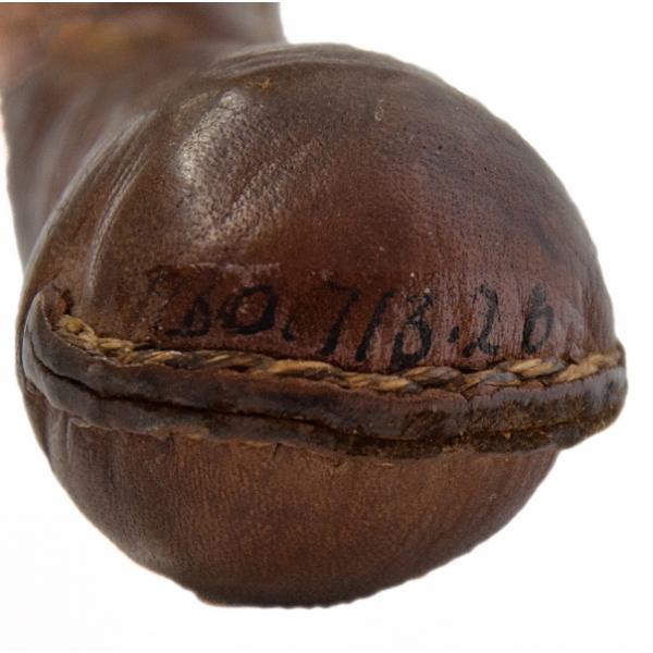 The end of a club covered in cracked brown leather, shaped like a ball. There is a seam running horizontally along the middle that has been stitched with light-coloured thread.  