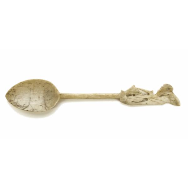 Front of ivory-carved spoon. The handle is carved and resembles a sitting figure. 