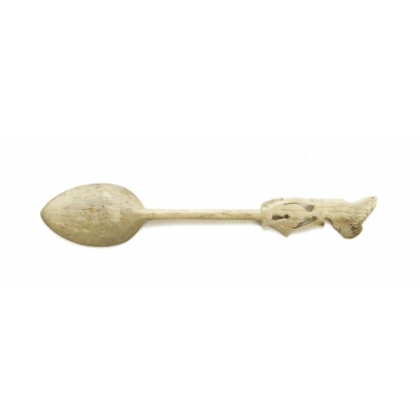 Back of ivory-carved spoon. The handle is carved and resembles a sitting figure.