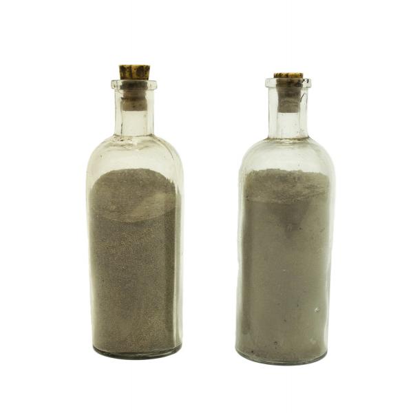 Two clear glass bottles filled with sand-coloured ash. The bottles are tall with a short spout and light brown corks in the tops.