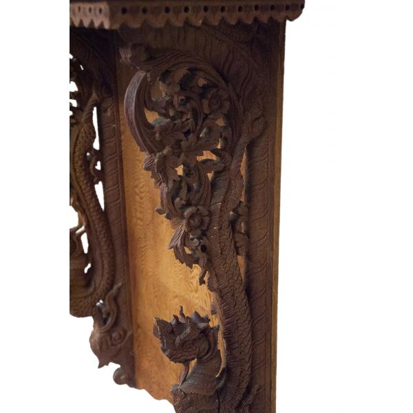 The bottom section of a brown wooden grandfather clock. There are dragons carved into the supports, with the heads at the bottoms and the tails curving up towards the clock platform. The tails ends in a floral design.