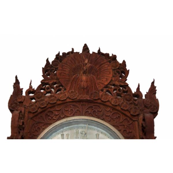 The top of a carved wooden clock. A peacock sits with its tail feathers spread out. There are flowers around the tail.