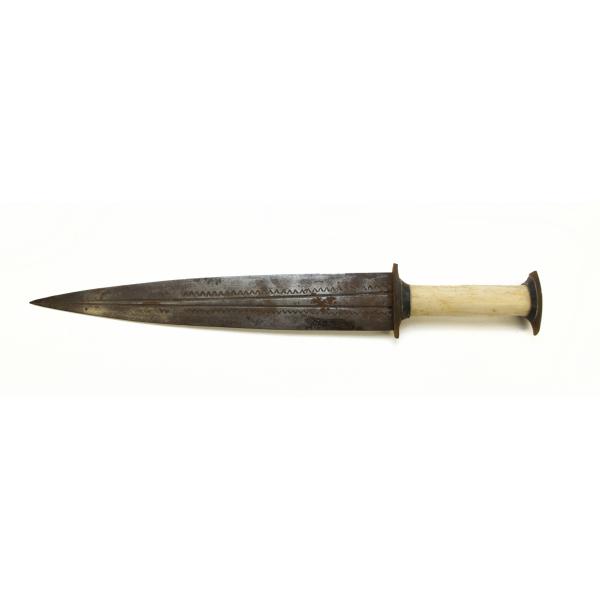 A metal dagger with an ivory handle pointing left. The blade is symmetrical and there are two grooves running the length of the blade. There is a "v" pattern towards the edge of the blade.