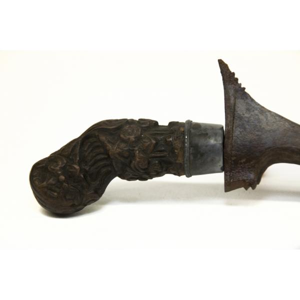 The carved wooden handle of a dagger. The wood is dark brown and it is decorated with lines and shapes.