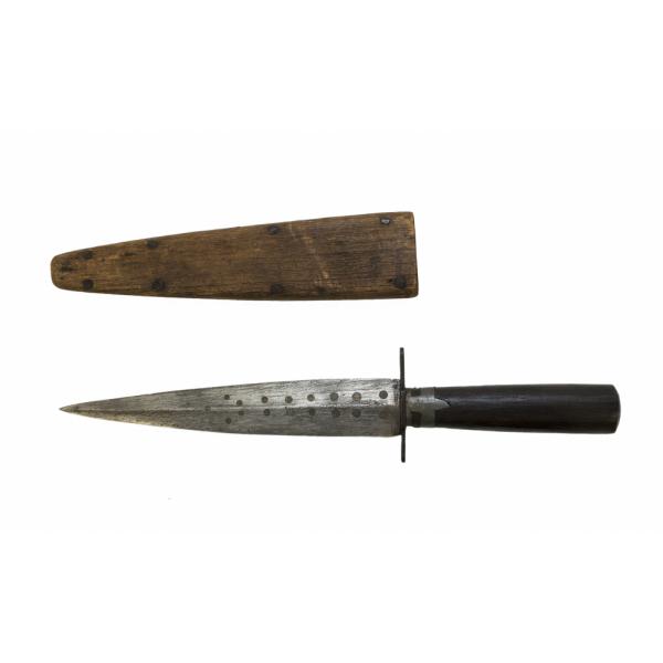 A metal dagger with a symmetrical blade and a wooden sheath, pointing to the left. The dagger has a dark wooden handle and two rows of dots along the blade. The brown wooden sheath has four nails on either side along the edge. 