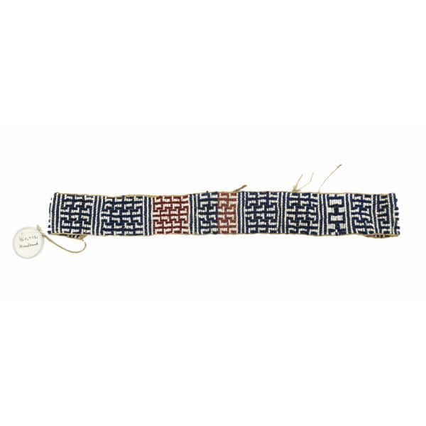 White, blue, and red beads woven into a geometric design, forming a rectangle. There is a piece of twine coming off of the left end that is attached to a white circular tag.