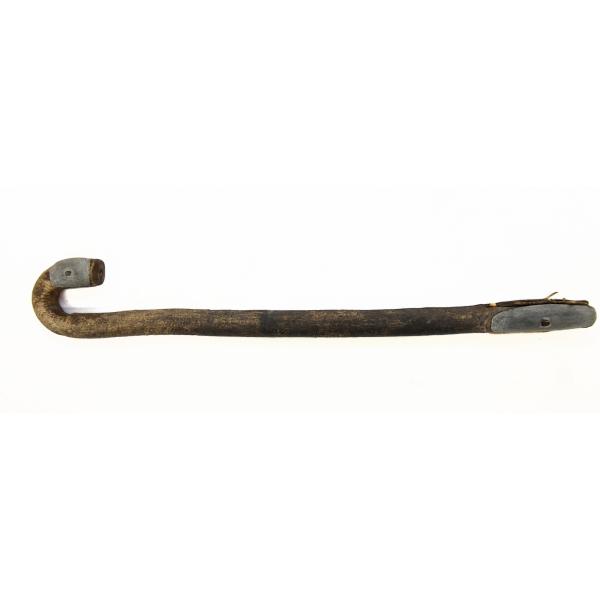 The handle of a wooden camel whip. It is curved like a cane. There is a piece of metal at each end of the handle. 