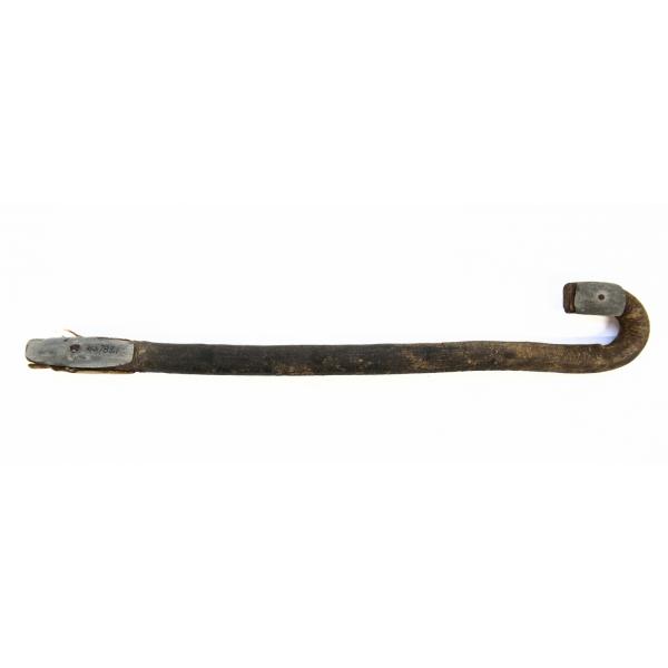 The handle of a wooden camel whip. It is curved like a cane. There is a piece of metal at each end of the handle. 