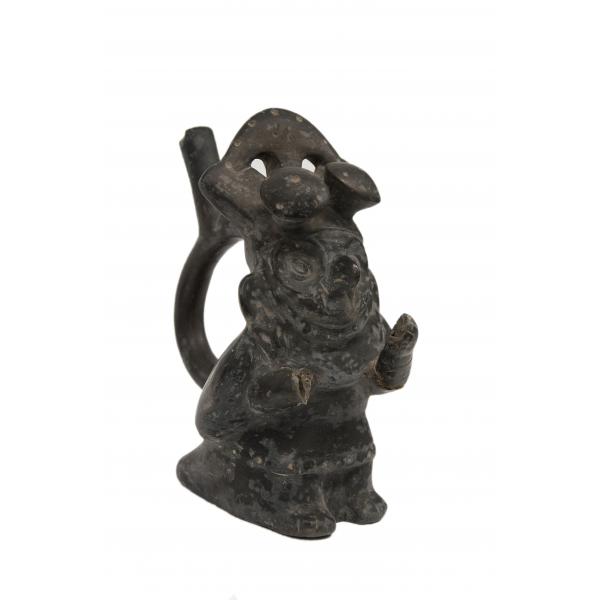 Side of the black stirrup-spout vessel shaped like a bird. The spout is visible at the back of the figure. The wings and feet can be seen, as well as the right side of the face.  