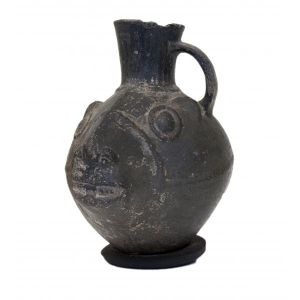 Side view of black stirrup-handle jug, shaped like a llama's head. 