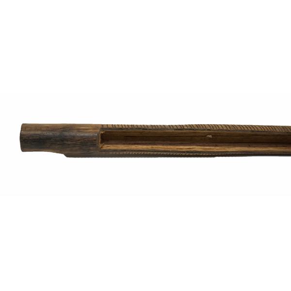 A brown reed instrument with carved bands along its body. There is a groove cut out on top between the mouthpiece and the end. The end is smooth and there is a notch carved out of it.  