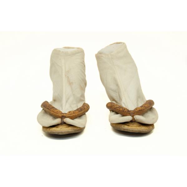 A pair of light brown flat thong sandals. There are white socks with a split toe to allow the toes to sit on either side of the thong.  