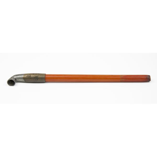 Une pipe à opium faite de bois orange. Une pièce métallique se trouve à l’extrémité. Une partie de celle-ci est de couleur argent. L’autre est dorée et des caractères japonais y sont gravés. 