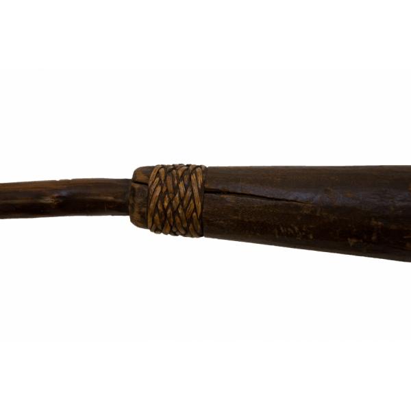 The handle of a stick used for protection. It is made from dark brown wood and there is a twine pattern on the bottom of the handle where it connects to the shaft. 