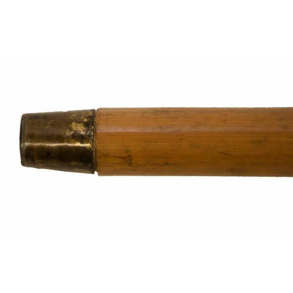 The base of a bamboo cane. There is a piece of brass-coloured metal on the bottom. The shaft of the cane is brown and smooth. 