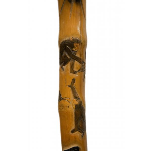 Two monkeys, one above the other, carved onto the shaft of a walking cane and then painted brown. One is crouched and the other is reaching up towards the first. 