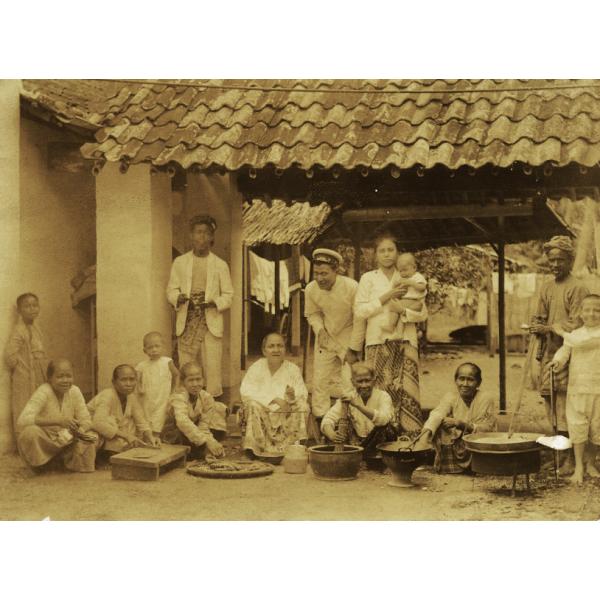 A group of people under an open structure with a tiled roof. There are boards and bowls in front of them and they are preparing food. 