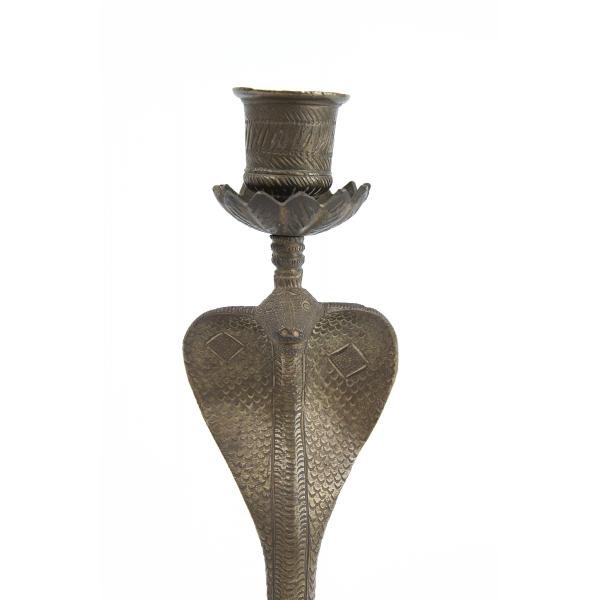 The head of a cobra-shaped candlestick. It has a scale pattern etched into it. The candle holder sits on tops of a base coming up from the cobra's head and is decorated with diagonal lines.