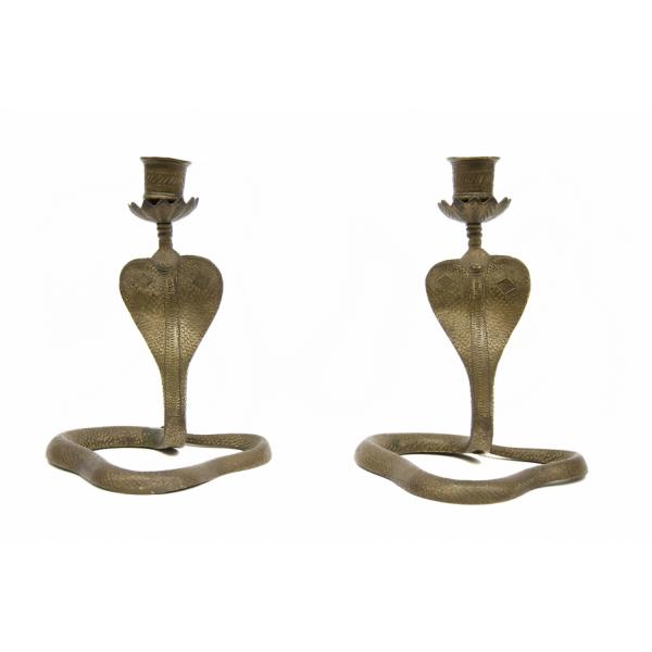 Pair of matching candlesticks in the shape of a cobra snake with its head raised. The candlesticks have been incised with a scale pattern. The candle holder sits on tops of a base coming up from the cobra's head and is decorated with diagonal lines.