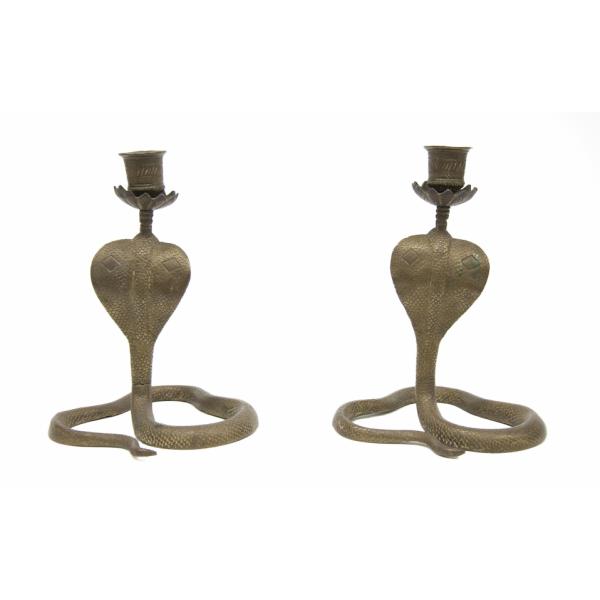 Back of a pair of matching candlesticks in the shape of a cobra snake with its head raised. The candlesticks have been incised with a scale pattern. The candle holder sits on tops of a base coming up from the cobra's head and is decorated with diagonal lines. 