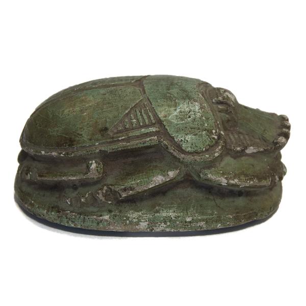 Side view of a green-painted scarab, facing right. The shell and legs are visible. 