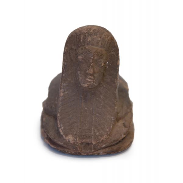  The front of a brown ceramic, human-headed scarab. Eyes, ears, a nose, and a mouth have been etched into the figure's head along with a headdress. 