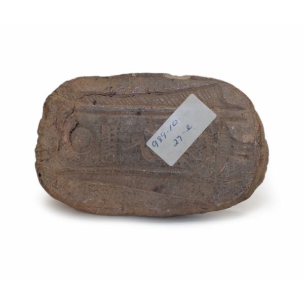 The underside of a brown ceramic human-headed scarab showing the inscribed cartouche. 