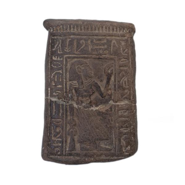 The front of a ceramic stele with a figure crouched in adoration, surrounded by an inscription of hieroglyphics.   