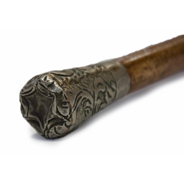 A brass handle from a maple-coloured walking cane. The initials "J.G." have been etched into it and are surrounded by curved lines.